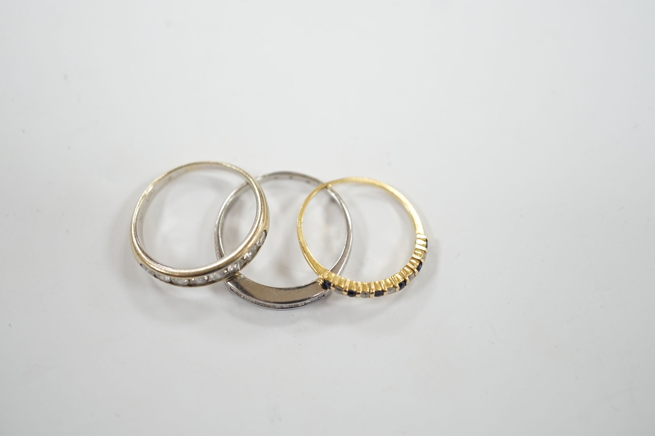 A white metal (stamped 950) and thirteen stone channel set baguette cut diamond ring, size O, together with two other unmarked gem set rings including diamond half eternity ring.